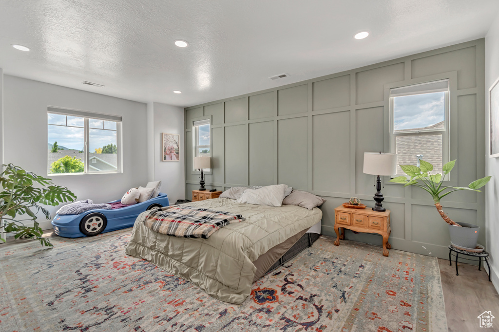 Bedroom with a decorative wall, recessed lighting, and wood finished floors