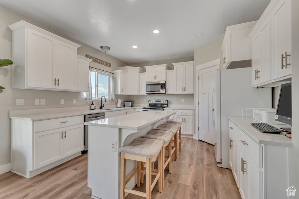 Kitchen featuring stainless steel appliances, light wood-type flooring, a kitchen breakfast bar, white cabinetry, and recessed lighting