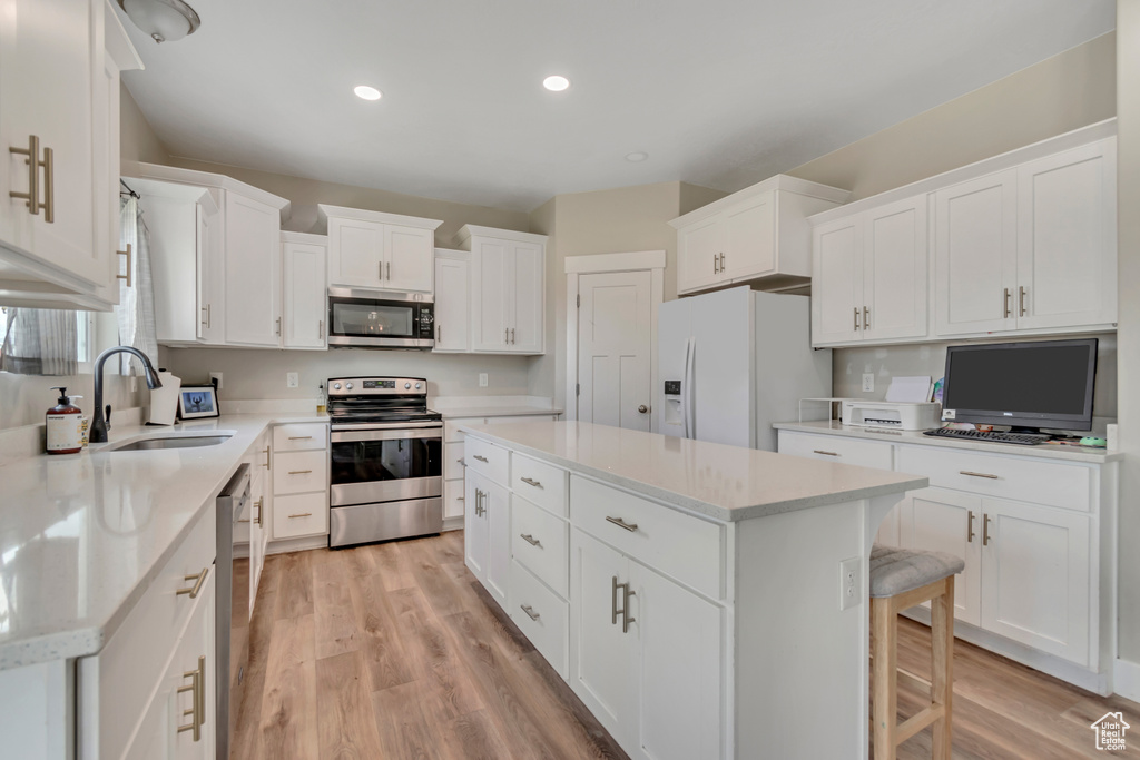 Kitchen with stainless steel appliances, a kitchen island, light wood-style flooring, white cabinetry, and recessed lighting