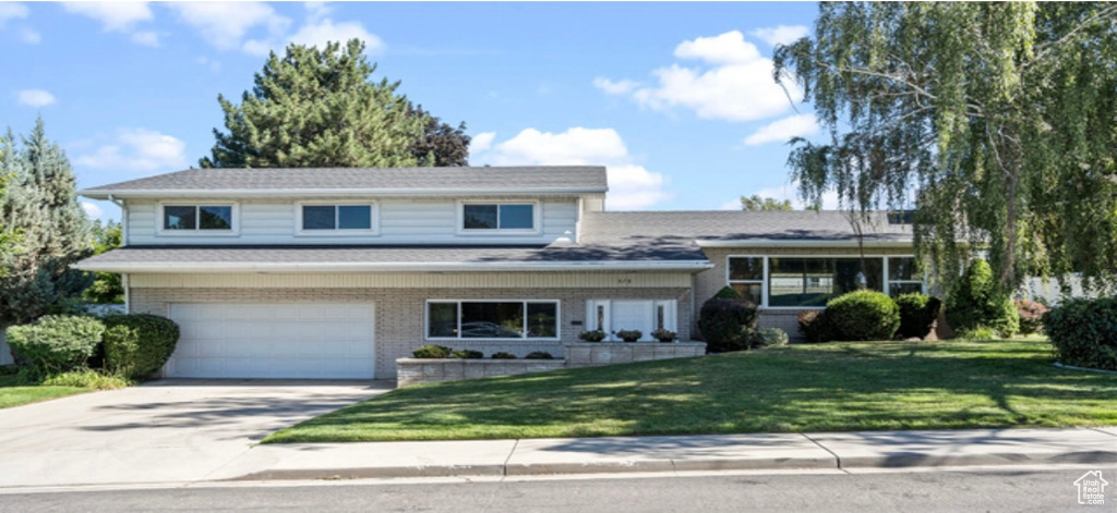 Tri-level home featuring concrete driveway, an attached garage, a front lawn, and brick siding