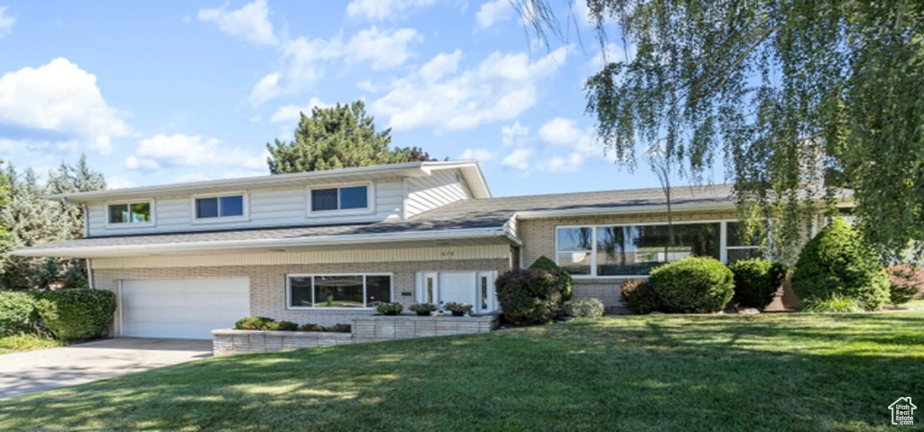 Split level home with brick siding, driveway, a front lawn, and an attached garage