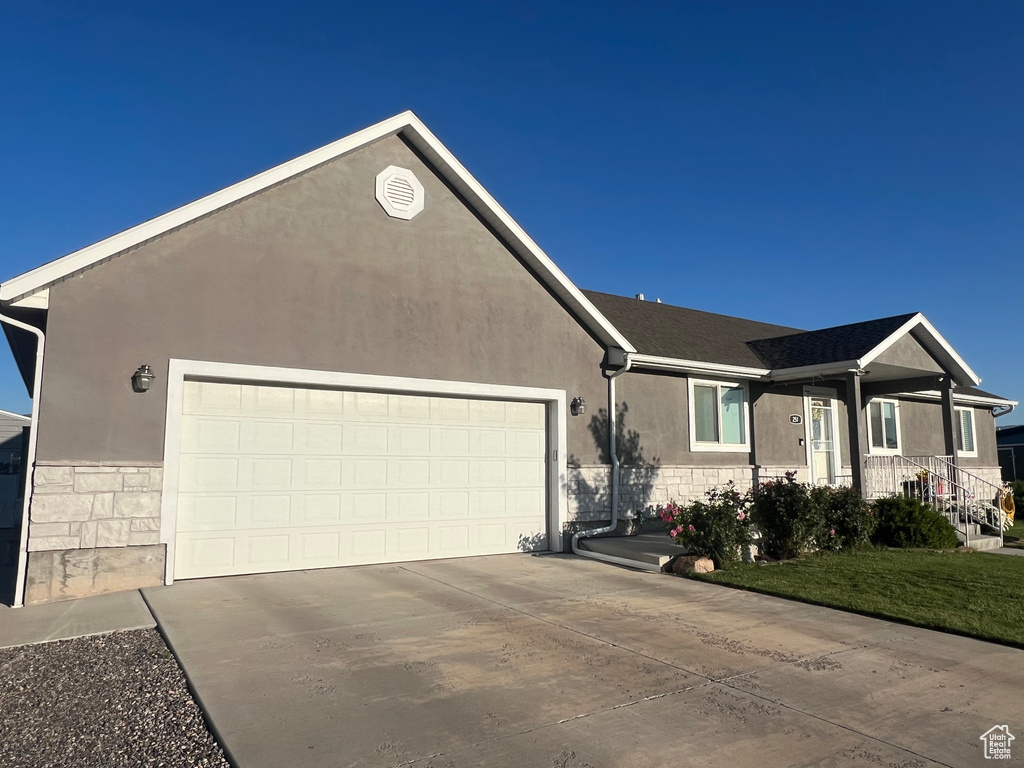 Single story home with an attached garage, concrete driveway, stucco siding, and stone siding