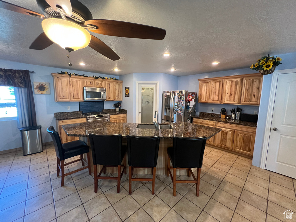 Kitchen featuring appliances with stainless steel finishes, a kitchen breakfast bar, a textured ceiling, a kitchen island with sink, and light tile patterned floors