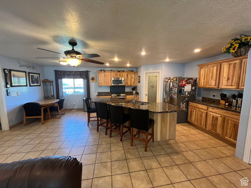 Kitchen featuring appliances with stainless steel finishes, light tile patterned floors, a breakfast bar, a center island with sink, and a textured ceiling