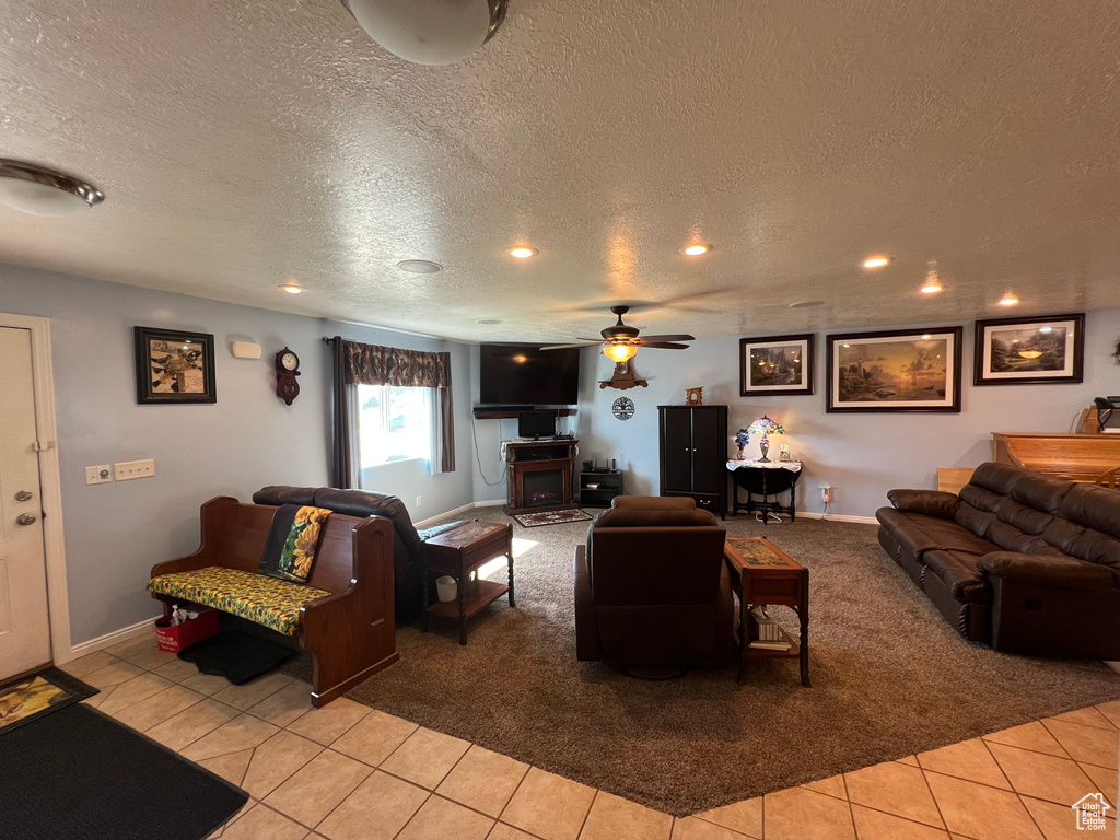 Living room featuring light colored carpet, a textured ceiling, a ceiling fan, light tile patterned floors, and a fireplace