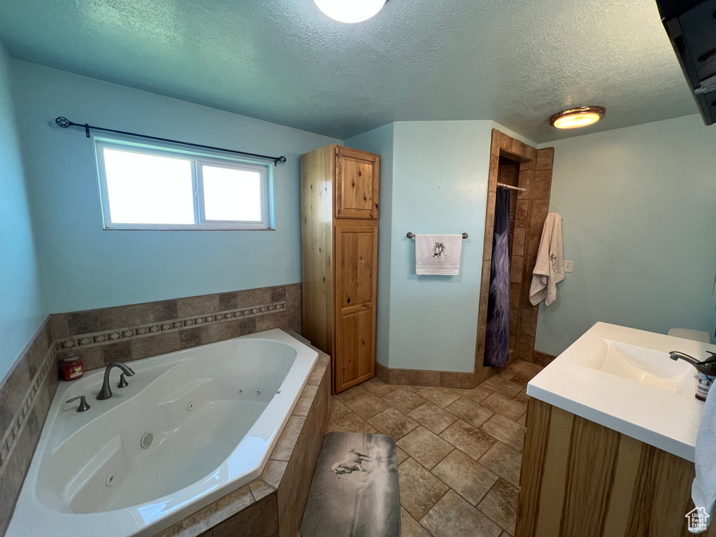 Bathroom featuring a textured ceiling, a jetted tub, a tile shower, and vanity