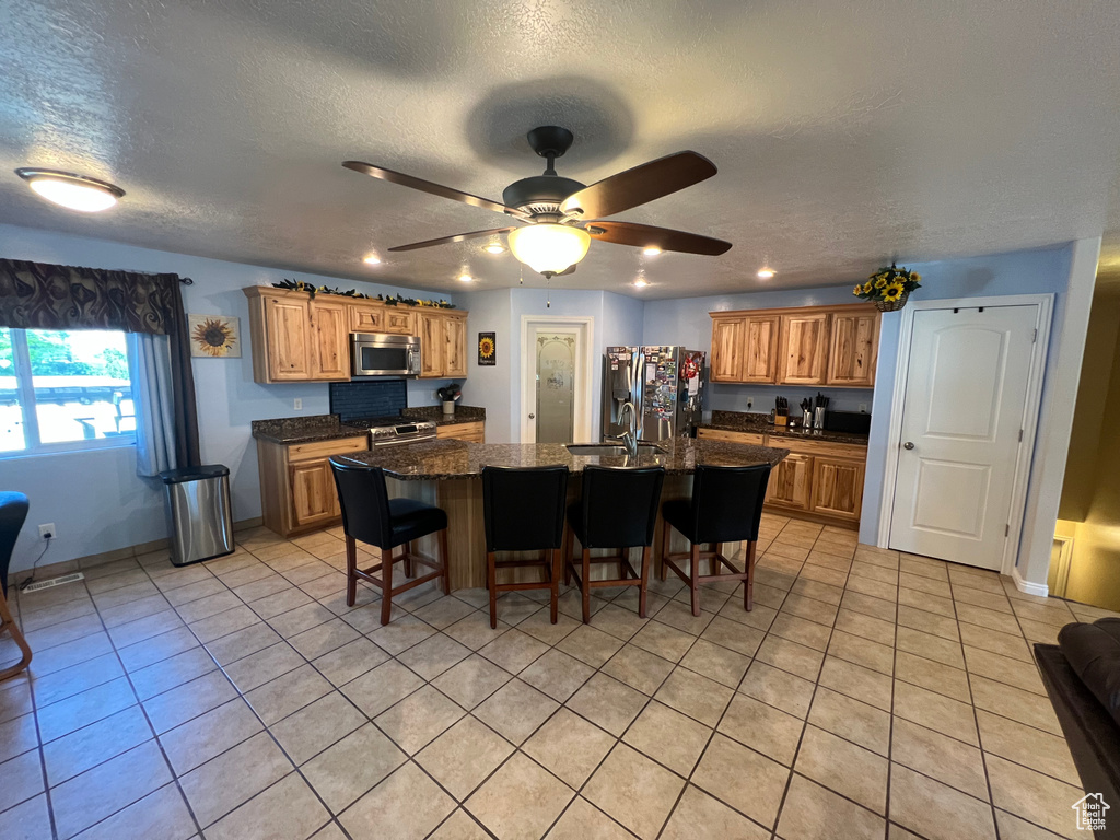 Kitchen featuring appliances with stainless steel finishes, a kitchen breakfast bar, light tile patterned floors, a center island with sink, and a textured ceiling