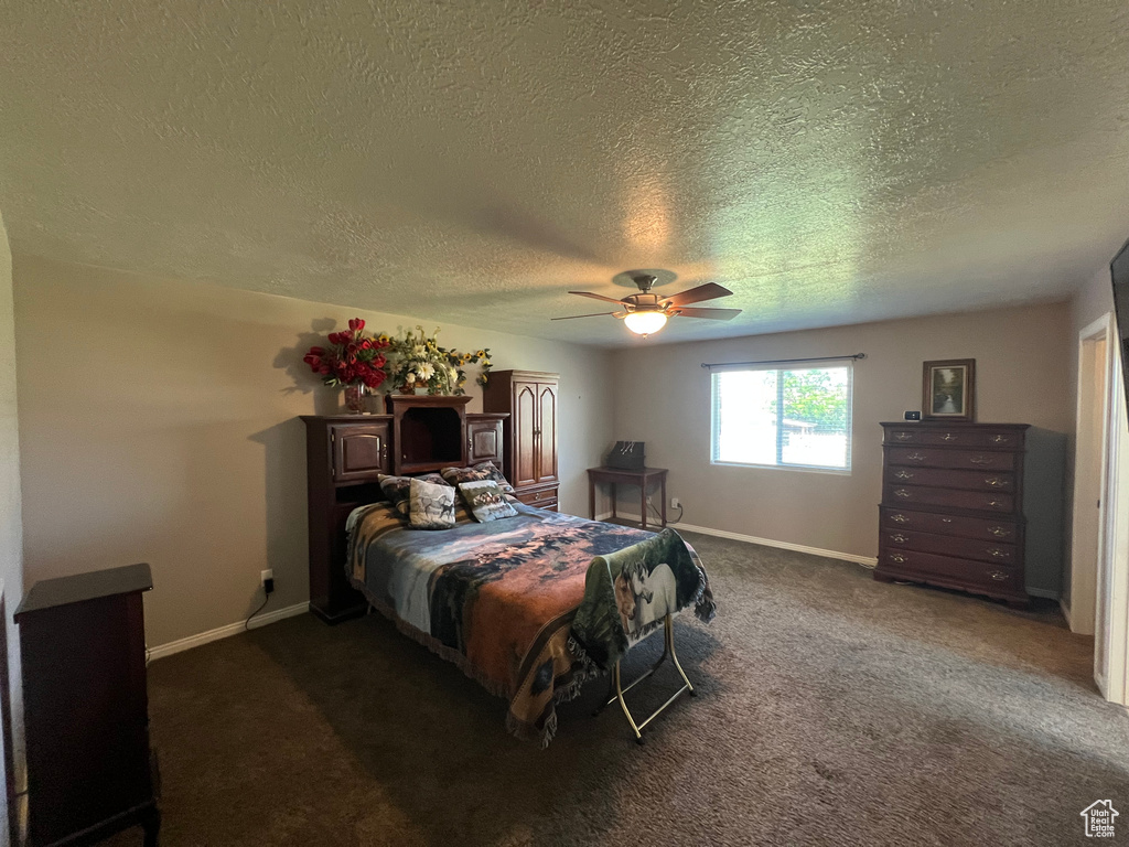 Bedroom with a textured ceiling, dark carpet, and a ceiling fan