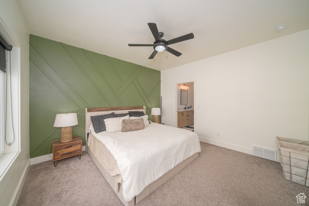 Bedroom featuring light colored carpet, a ceiling fan, a decorative wall, and ensuite bathroom