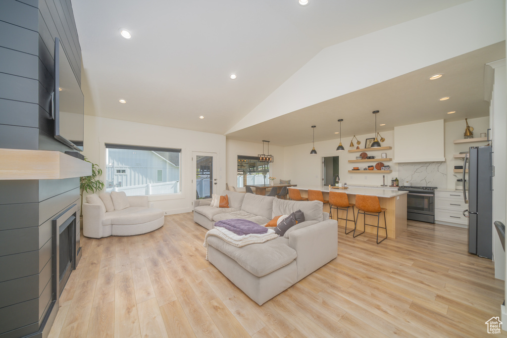 Living area with light wood finished floors, recessed lighting, high vaulted ceiling, and a fireplace