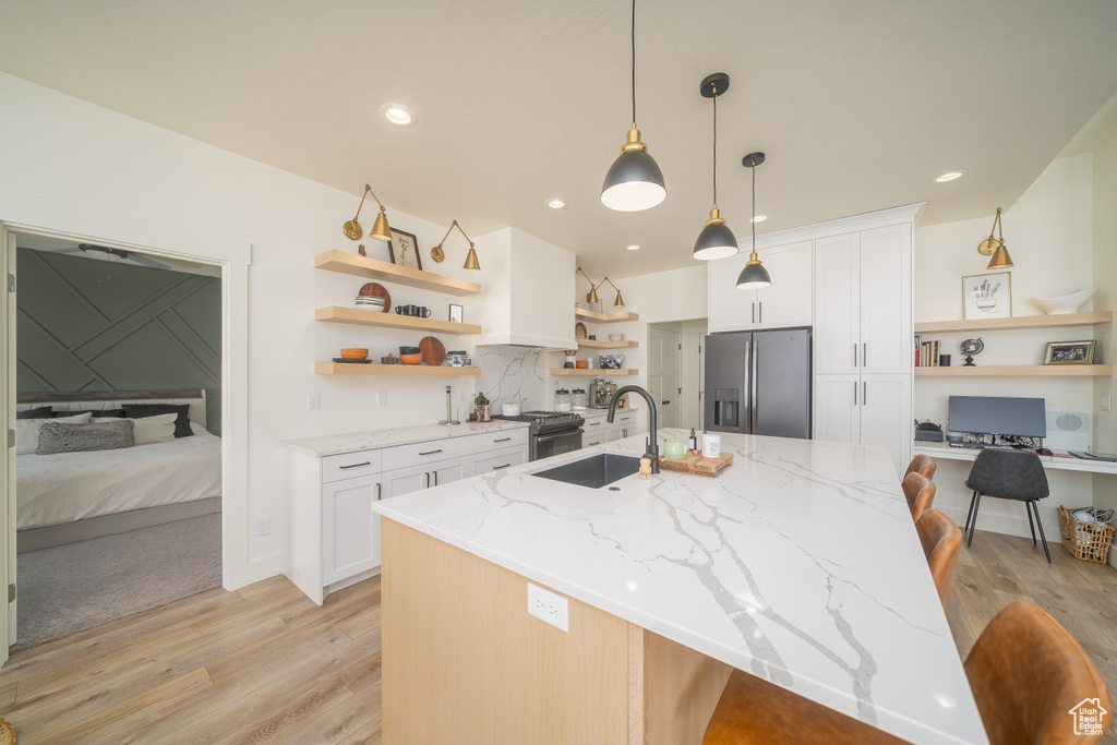 Kitchen featuring open shelves, stainless steel refrigerator with ice dispenser, light wood finished floors, white cabinetry, and a breakfast bar