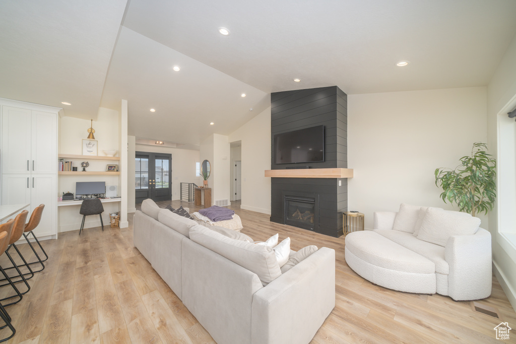 Living room featuring light wood-type flooring, a fireplace, recessed lighting, vaulted ceiling, and built in desk