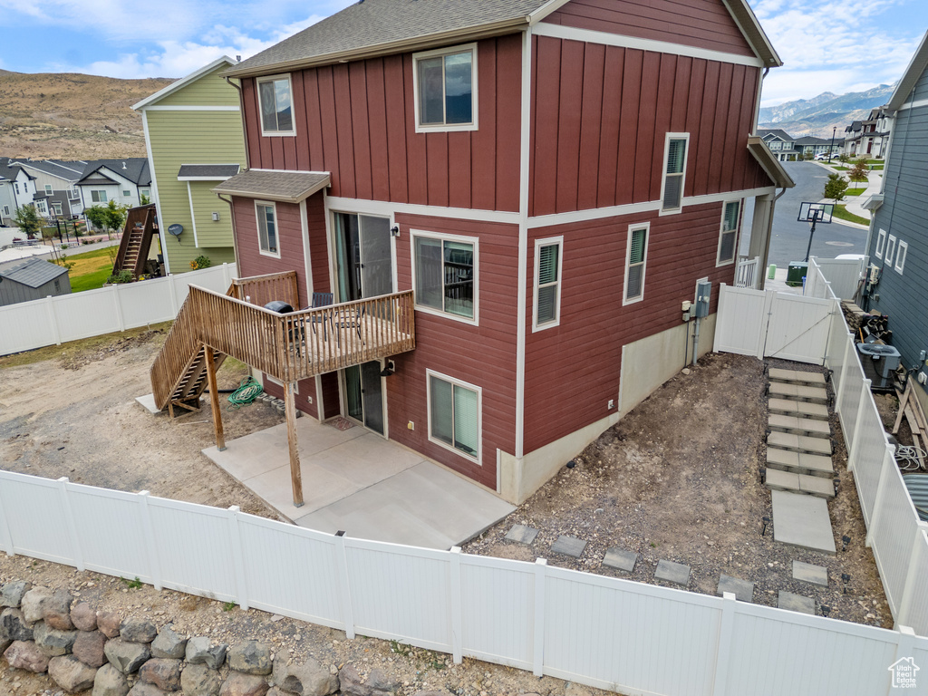 Back of property featuring a deck with mountain view, a fenced backyard, stairs, a patio, and board and batten siding
