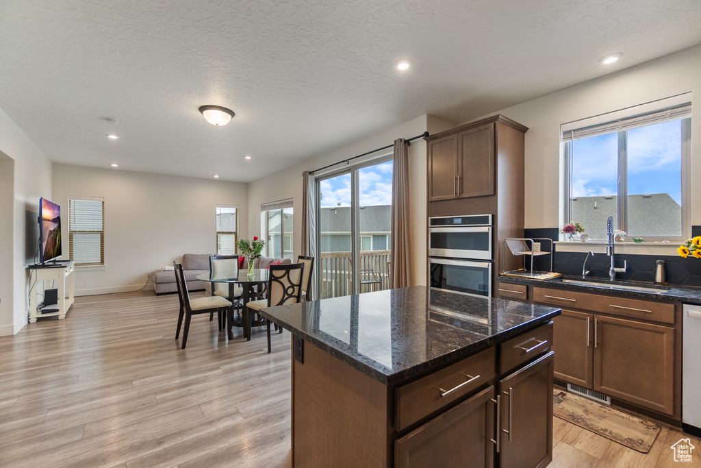 Kitchen featuring stainless steel double oven, light wood-type flooring, healthy amount of natural light, open floor plan, and recessed lighting