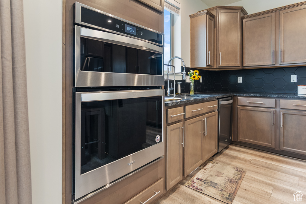 Kitchen with appliances with stainless steel finishes, light wood-style flooring, decorative backsplash, and dark stone countertops