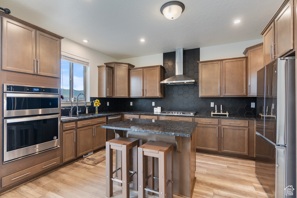 Kitchen featuring wall chimney exhaust hood, stainless steel appliances, light wood-style flooring, a kitchen island, and recessed lighting