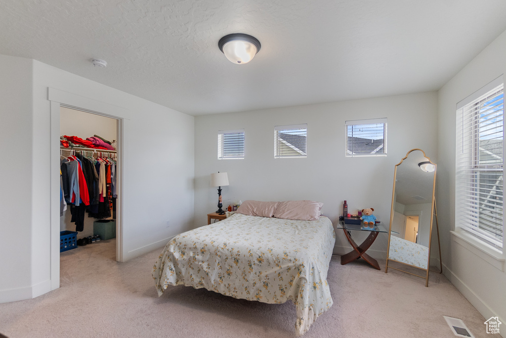 Bedroom with light colored carpet, a walk in closet, and a closet