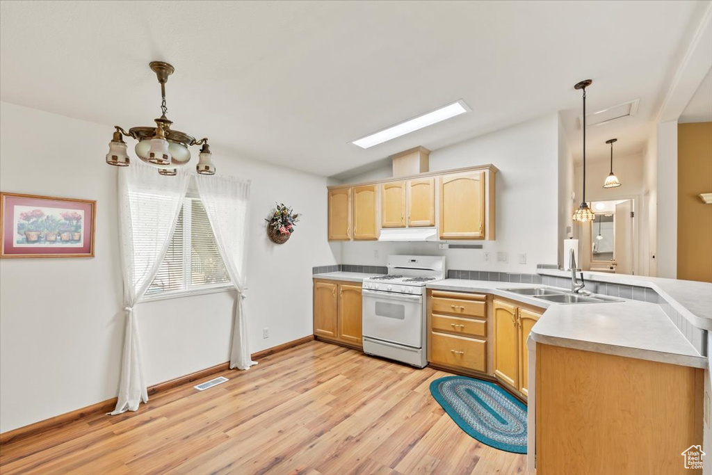 Kitchen with white gas range oven, under cabinet range hood, a chandelier, a peninsula, and vaulted ceiling