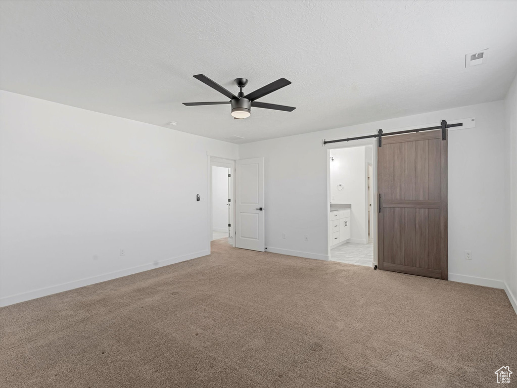 Unfurnished bedroom featuring a barn door, light carpet, ensuite bathroom, and a ceiling fan