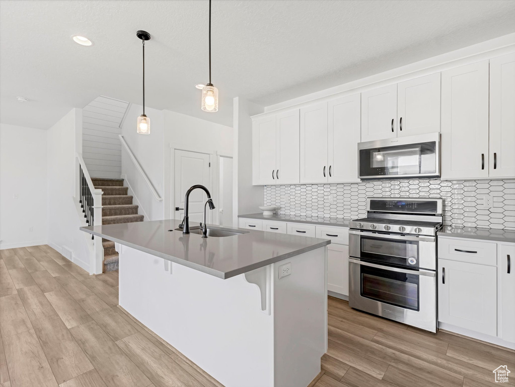 Kitchen featuring appliances with stainless steel finishes, decorative backsplash, light wood finished floors, white cabinets, and recessed lighting