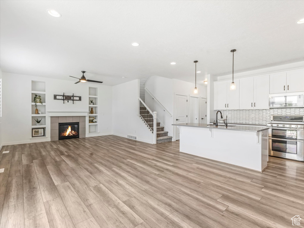 Unfurnished living room with stairway, light wood finished floors, a ceiling fan, built in shelves, and recessed lighting