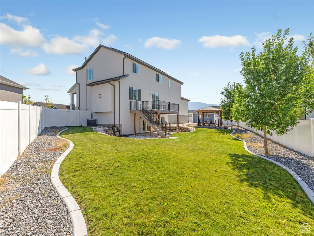 Back of house with a fenced backyard, a gazebo, stairs, and stucco siding