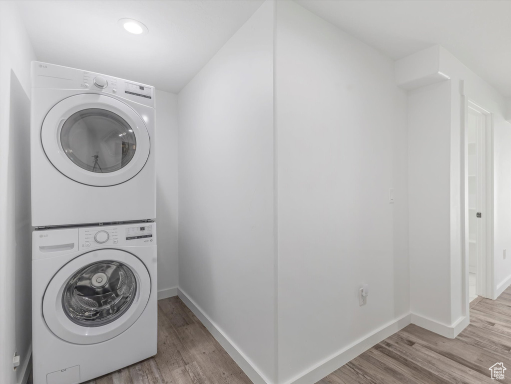Washroom with stacked washer and clothes dryer, light wood finished floors, and recessed lighting