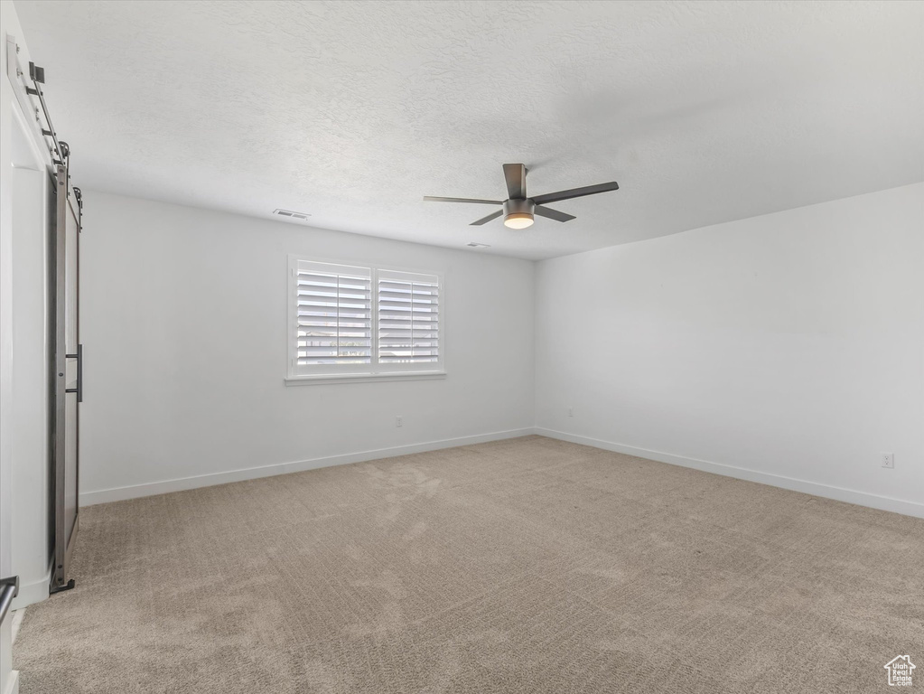 Empty room with a ceiling fan, light colored carpet, and a textured ceiling
