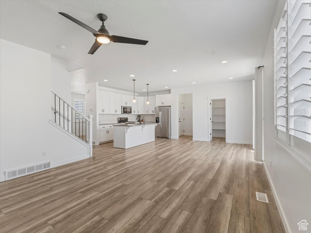 Unfurnished living room with a ceiling fan, light wood finished floors, recessed lighting, and stairway