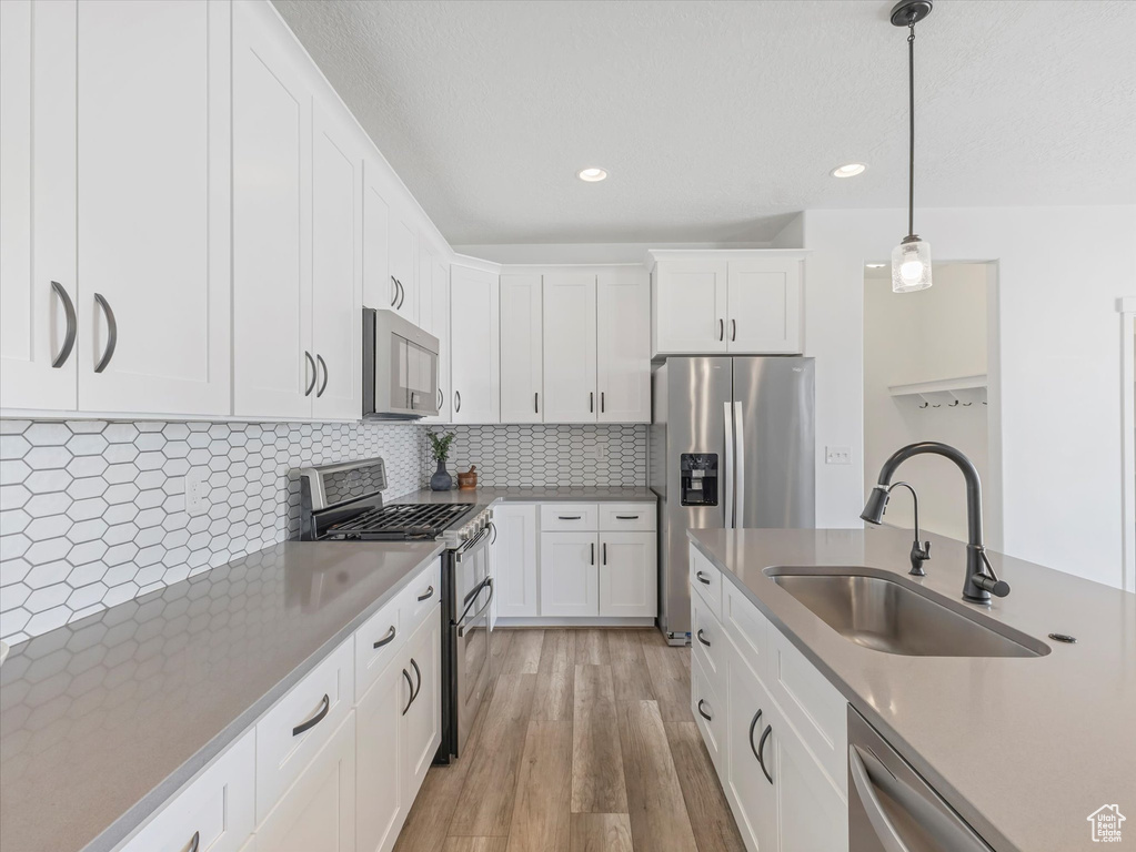 Kitchen with stainless steel appliances, white cabinets, pendant lighting, light wood-style floors, and recessed lighting