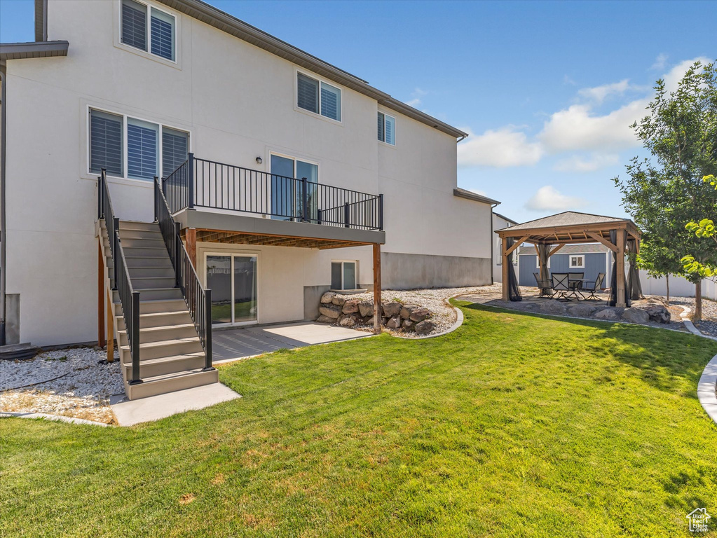 Back of house with a gazebo, a patio area, stucco siding, a yard, and stairs