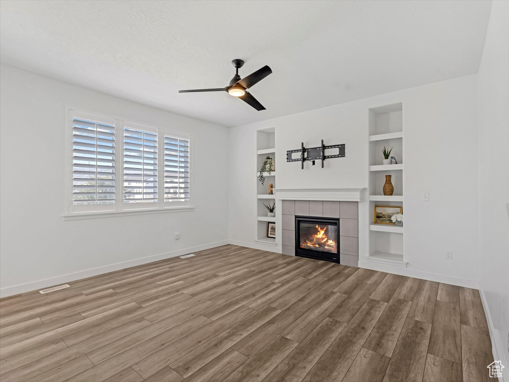 Unfurnished living room with wood finished floors, a tile fireplace, a ceiling fan, and built in features