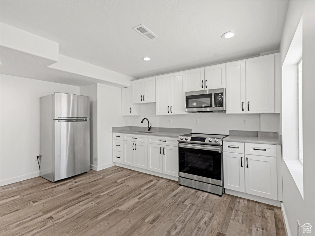 Kitchen with stainless steel appliances, light wood-type flooring, white cabinets, light countertops, and recessed lighting