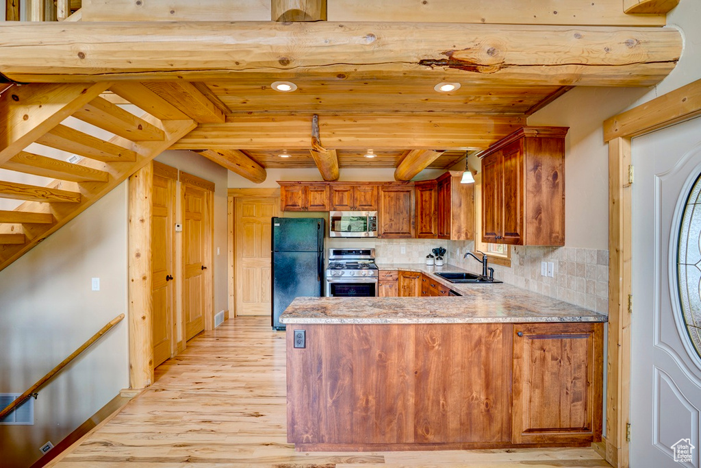 Kitchen with appliances with stainless steel finishes, brown cabinets, a peninsula, light wood-style flooring, and recessed lighting