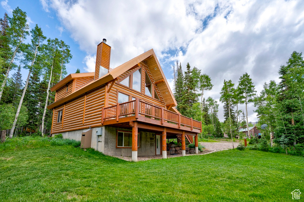 Rear view of house with a deck, a lawn, log veneer siding, and a chimney