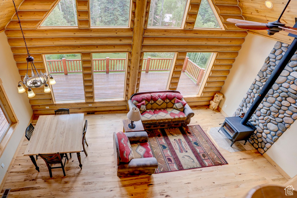 Living room with rustic walls, a wood stove, wood-type flooring, plenty of natural light, and a high ceiling