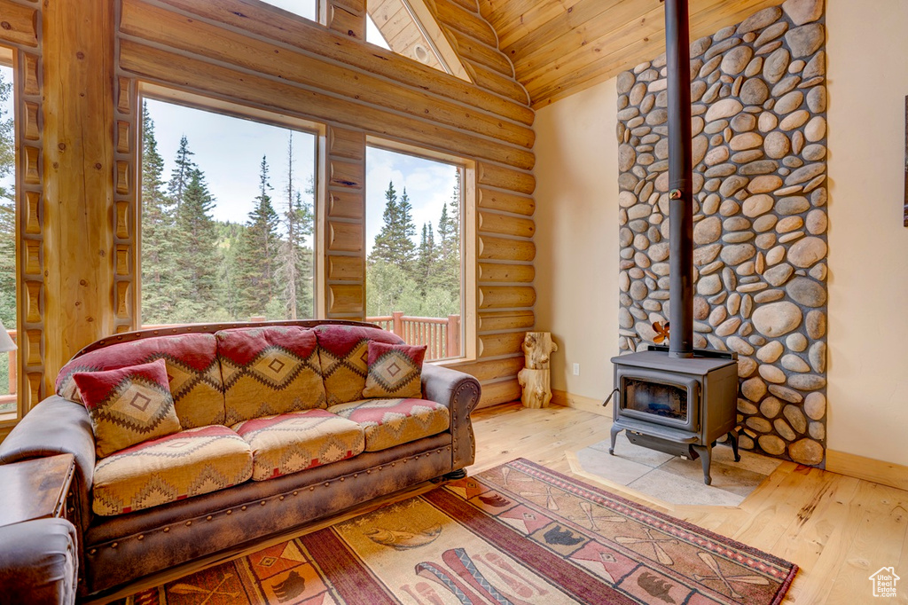 Living area with rustic walls, healthy amount of natural light, a wood stove, hardwood / wood-style floors, and high vaulted ceiling