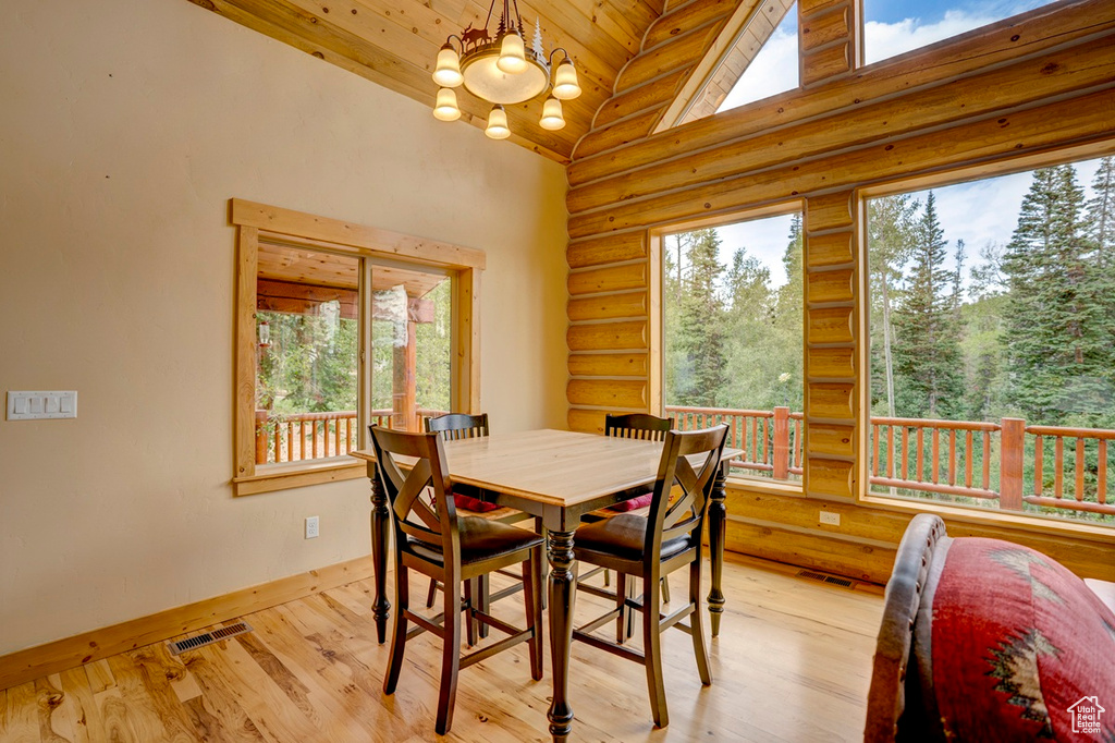 Dining space with rustic walls, plenty of natural light, a chandelier, light wood finished floors, and wood ceiling