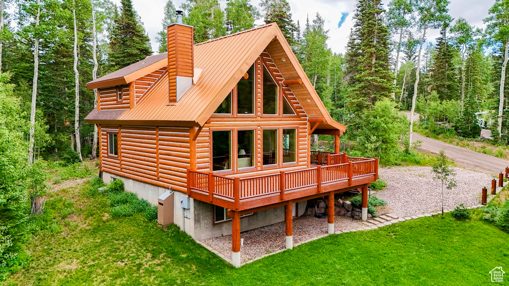 Rear view of property with a wooden deck, a yard, a chimney, and a metal roof
