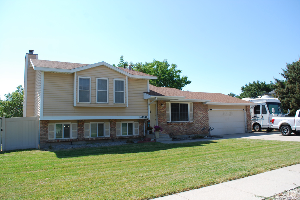 Tri-level home featuring brick siding, an attached garage, driveway, and a chimney