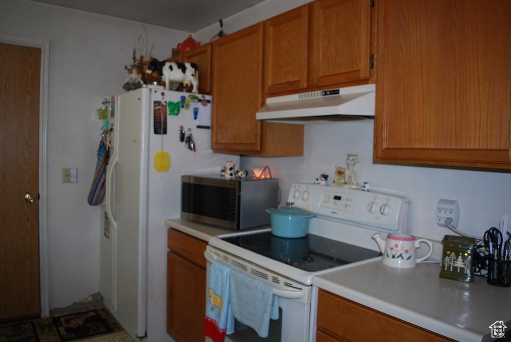 Kitchen with electric range, under cabinet range hood, stainless steel microwave, brown cabinetry, and light countertops