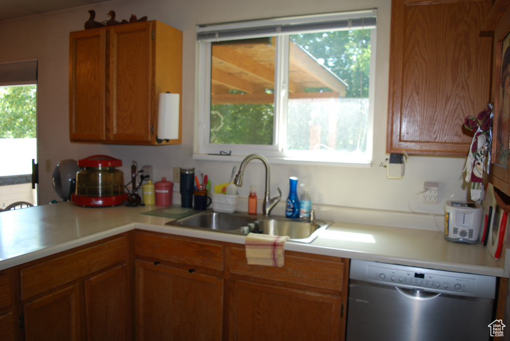 Kitchen with stainless steel dishwasher, light countertops, and brown cabinets