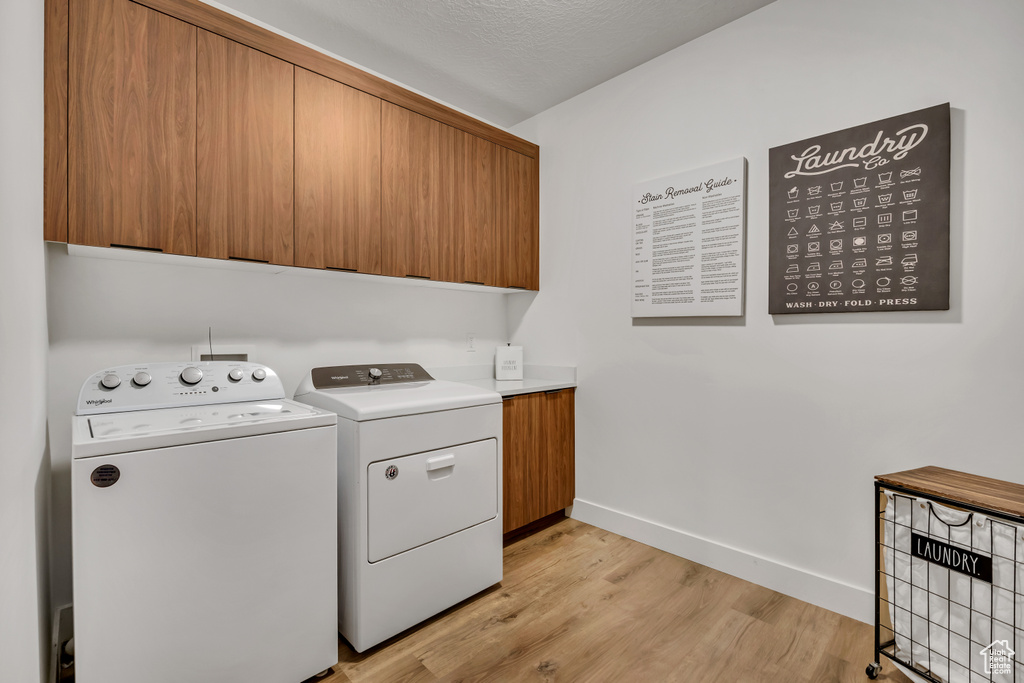 Washroom with washer and dryer, cabinet space, light wood finished floors, and a textured ceiling