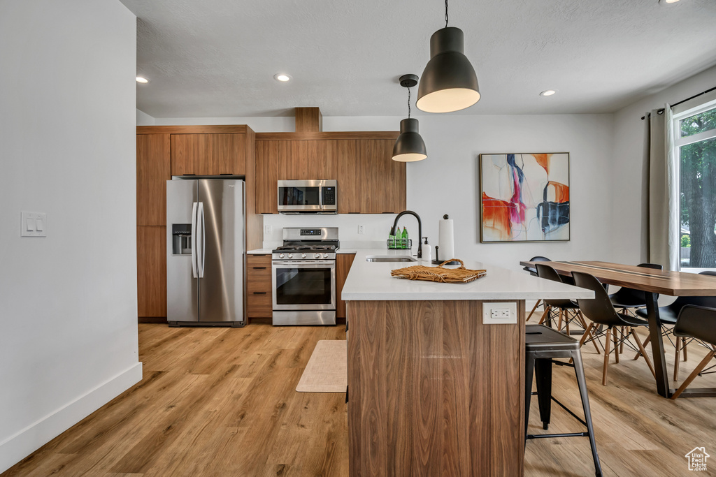 Kitchen featuring appliances with stainless steel finishes, brown cabinets, light countertops, a peninsula, and light wood-style floors