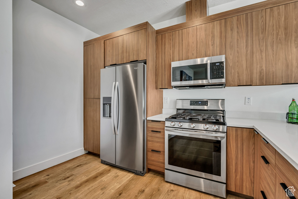 Kitchen featuring stainless steel appliances, brown cabinetry, light countertops, light wood finished floors, and recessed lighting