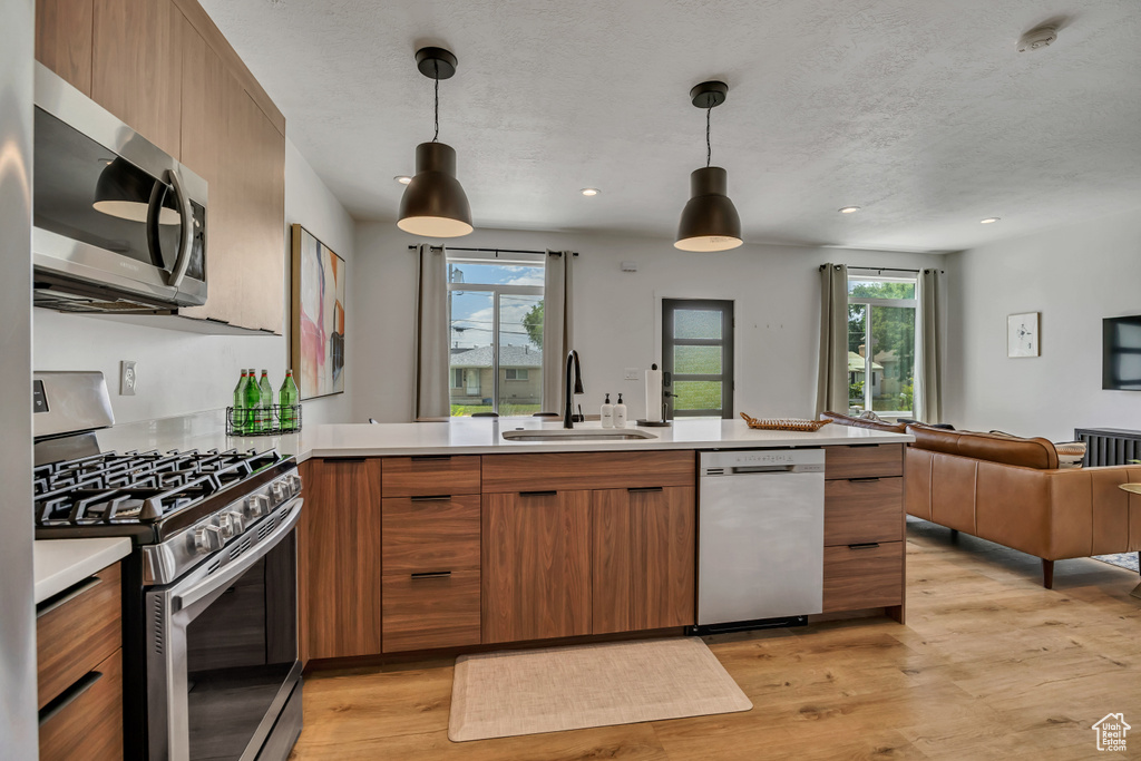 Kitchen featuring stainless steel appliances, open floor plan, light countertops, brown cabinetry, and recessed lighting