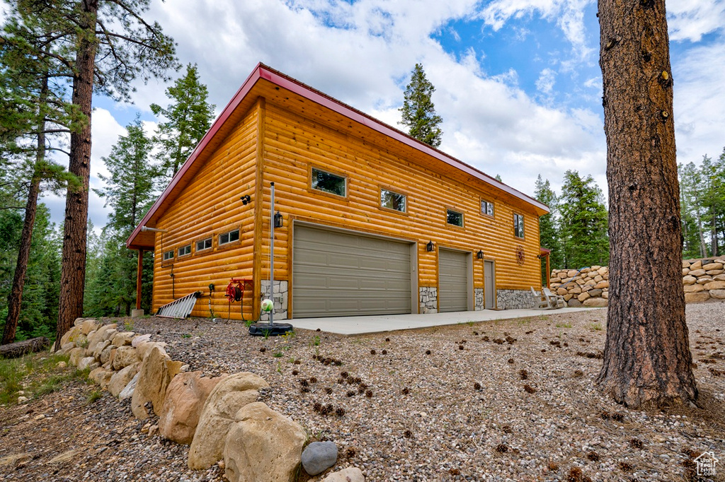 View of property exterior featuring log veneer siding, a garage, and driveway