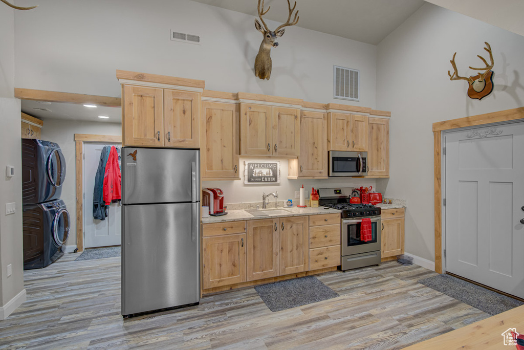 Kitchen with stainless steel appliances, stacked washer and clothes dryer, high vaulted ceiling, light brown cabinets, and light countertops
