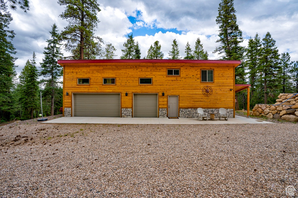 View of front of house with a patio area, gravel driveway, a garage, and stone siding