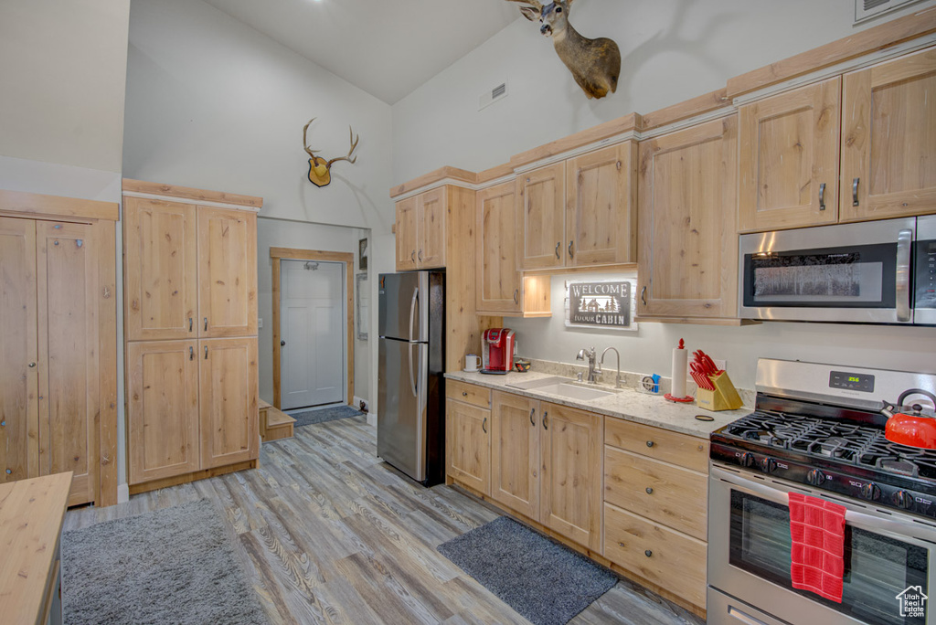 Kitchen with stainless steel appliances, light brown cabinets, high vaulted ceiling, and light wood finished floors